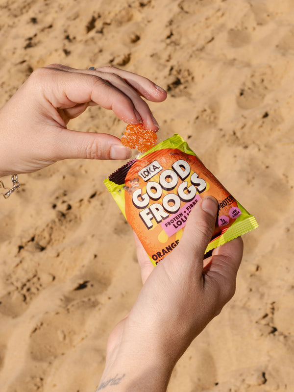 Hand grabbing a good frog protein lolly from a bag of orange sherbet lollies